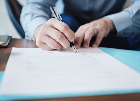 Business man at work in corporate office. Detail of hands of a busy manager signing documents and papers in a blue folder. Copy space.